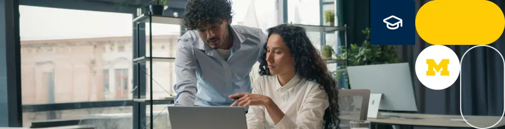 “Two individuals working in an office, one standing with a tablet and the other seated at a laptop.”

